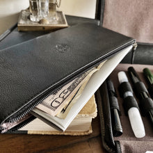 Load image into Gallery viewer, A Franklin-Christoph Currency Case - Leather holds cash and papers beside pens and a book on a wooden surface.