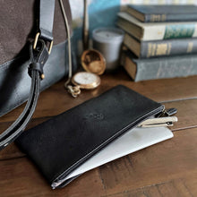 Load image into Gallery viewer, Franklin-Christoph Currency Case - Leather with pens sits on a notebook next to a bag, books, watch, and candle.