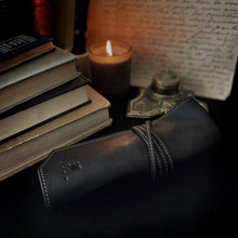 Load image into Gallery viewer, A Franklin-Christoph 5 Watch Roll in black leather &amp; suit grey sits beside books and a candle on the dark tabletop.
