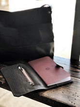 Load image into Gallery viewer, A Franklin-Christoph ETN - Black Napa w/ Suit Grey notebook rests open, pen ready, beside a sleek black bag in soft light.