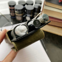 Load image into Gallery viewer, Close-up of three fountain pens in a Franklin-Christoph New Penvelope 3 NWF with ink bottles and books blurred behind.