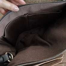 Load image into Gallery viewer, A hand opens a Franklin-Christoph Fortis Sling Bag—Iron Brown and Black—showing an empty, pocketed brown interior.
