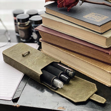 Load image into Gallery viewer, The Franklin-Christoph New Penvelope 3 NWF—a vegan case with removable slots—rests on a desk among books and ink bottles.