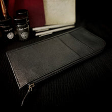 Load image into Gallery viewer, The Franklin-Christoph EDC Travel Wallet rests on a dark surface beside ink bottles and pens.