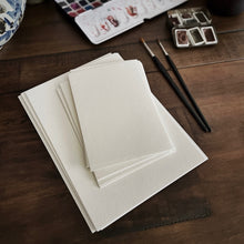 Load image into Gallery viewer, Franklin-Christoph Water Color Paper - Loose Leaf, two paintbrushes, and paint trays on a wooden table.