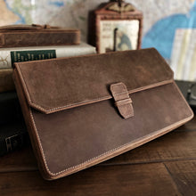 Load image into Gallery viewer, A Franklin-Christoph Penvelope 12 Boot Brown Leather sleeve and pen case rest on a desk with books and a vintage clock.