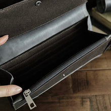 Load image into Gallery viewer, A hand opens an empty Franklin-Christoph Fortis Clutch Envelope - Iron Brown &amp; Black on a wooden surface.